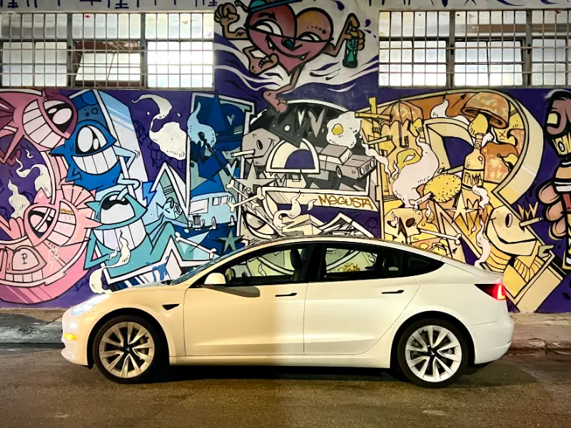 White Tesla Model 3 at night in front of a mural in Wynwood, Miami
