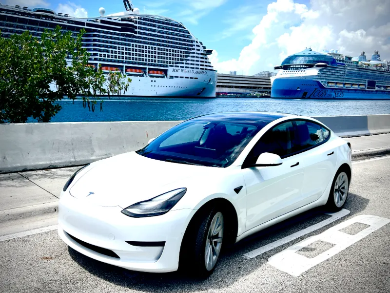 White Tesla Model 3 at PortMiami with cruise ships docked behind