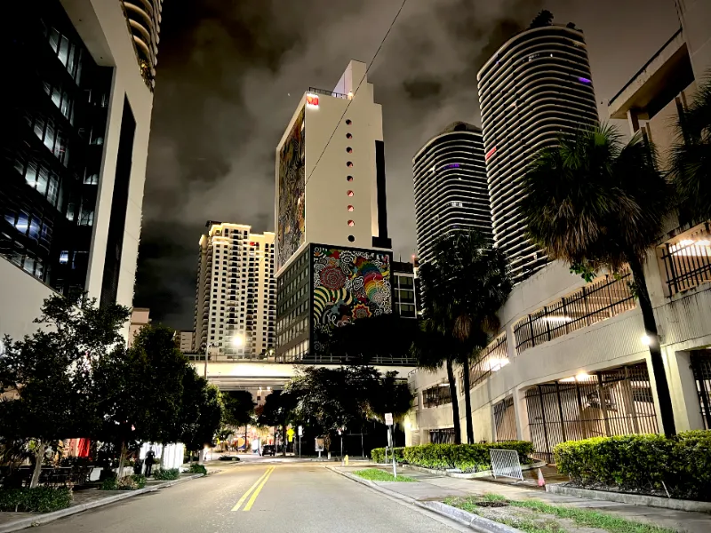 Brickell street at night below a mural high-rise and curved residential towers, Miami